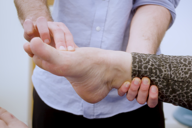 Image shows close up on foot and lower leg. Male nurse finds two pulse points at posterior tibial and the dorsalis pedis