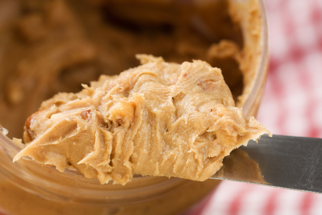 Close-up photo shows knife scooping peanut butter out of a jar