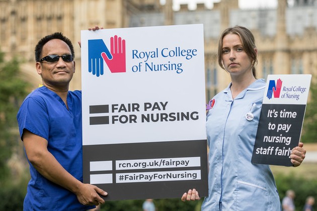 Two nursing staff holding a placard outside Westminster Houses of Parliament for RCN Fair Pay campaign