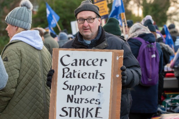 A patient attends an RCN picket line in January 2023 holding a sign saying 'Cancer patients support nurses strike'