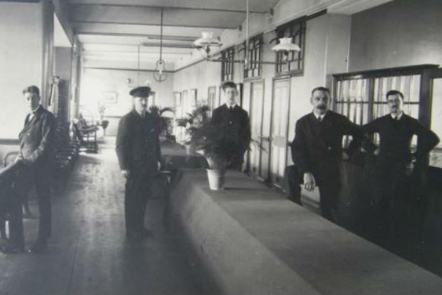 Black and white image shows five male nurses standing in a large corridor