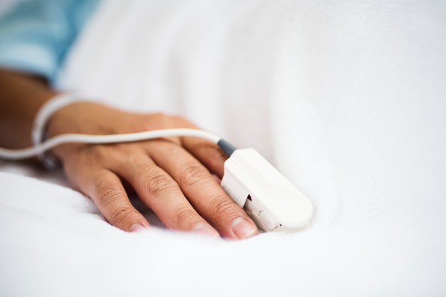 Close-up image of the hand of a patient in a hospital bed with a pulse oximeter on their finger