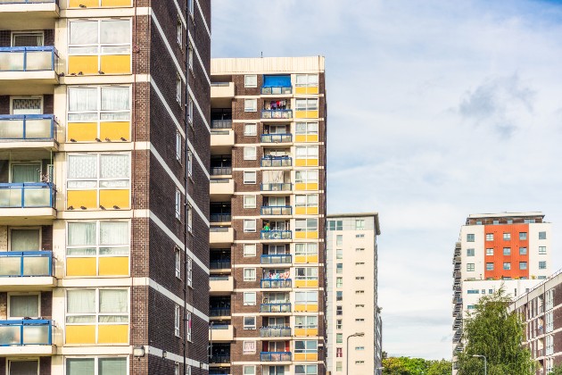 Council housing blocks shown on left of photo and other housing block on distance in right against blue sky