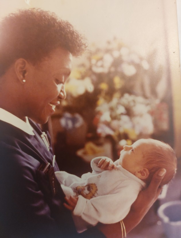 Allyson in community midwife uniform holding a baby 1980s