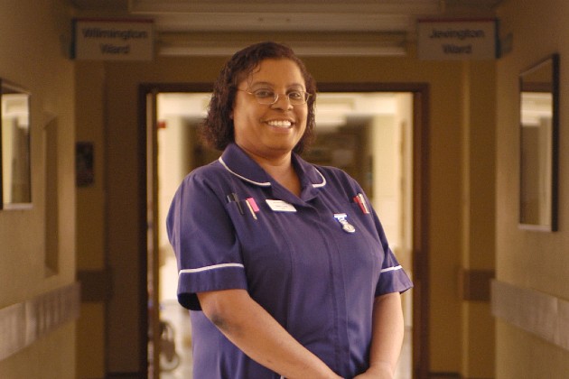 Dionne Daniel wearing dark purple sister's uniform smiling to camera in a hospital corridor 2004