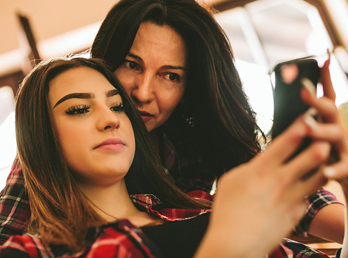 Mum leans lovingly over daughter's shoulder