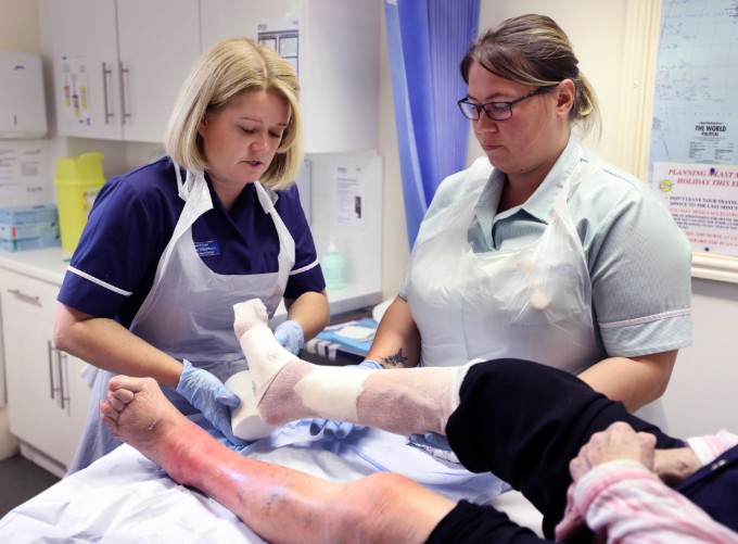 Nurse Emma and a healthcare support worker bandage a patient's leg during a wound care clinic