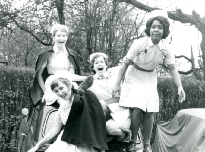 A group of four laughing nurses climb on a car