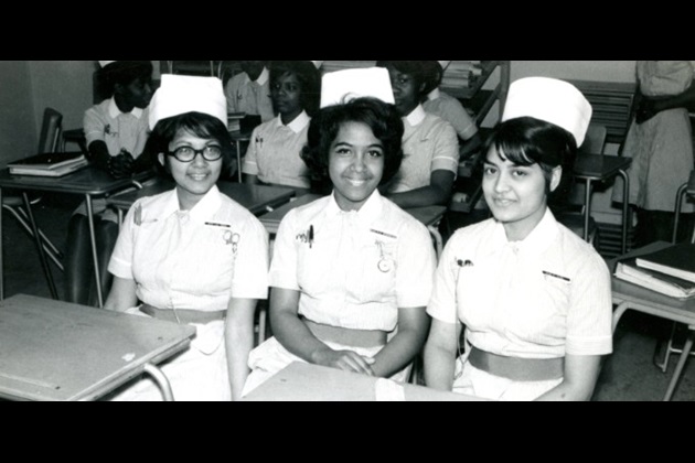 Three BAME nursing students sit together at desks in a classroom
