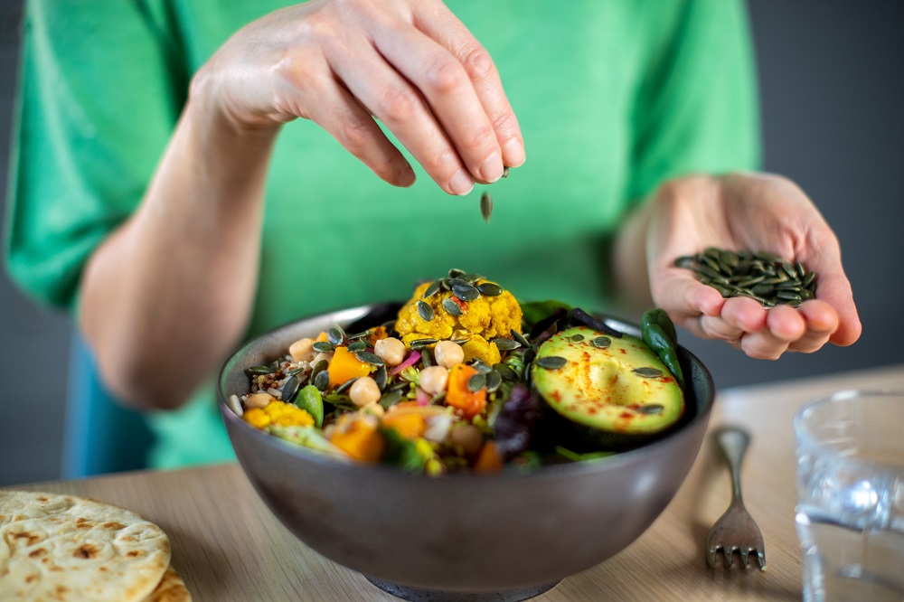 close up of someone sprinkling nuts on a bowl of salad