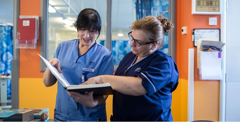 Two nurses in Scottish NHS uniforms reading a chart