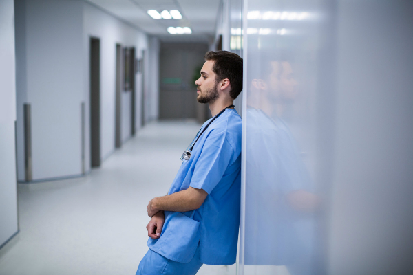 Image of tired male nurse leaning against a wall