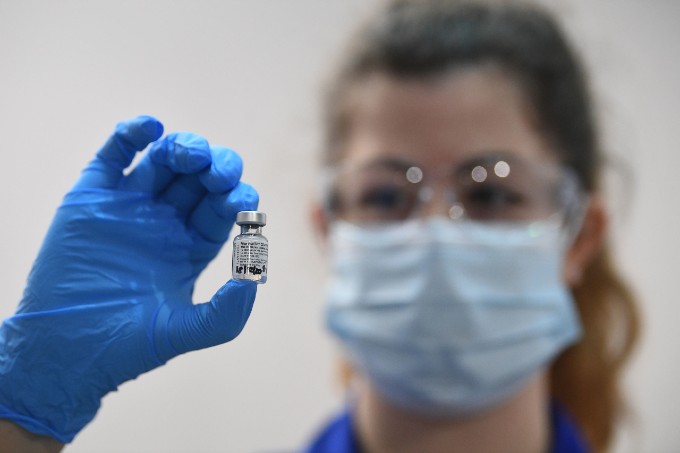 Woman in mask and gloves holds up vial of COVID-19 vaccine to the camera